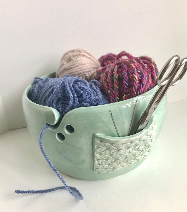 yarn and knitting needles in a bowl on a white surface with two crochet hooks