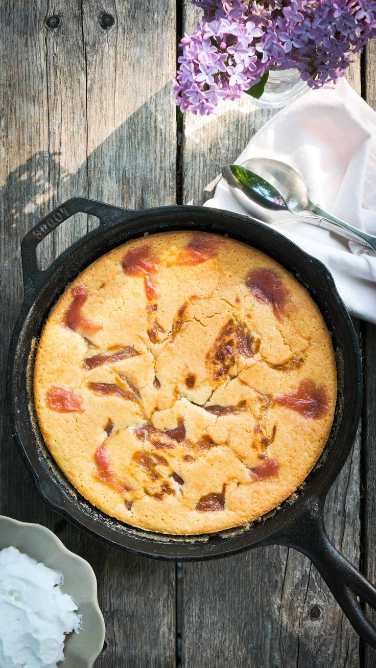 a skillet filled with food sitting on top of a wooden table next to purple flowers