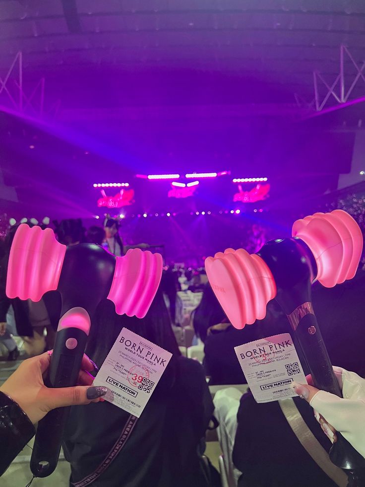 two women holding up wine bottles with pink lights on them in front of an audience