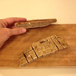 a person holding a piece of bread on top of a wooden cutting board next to a knife