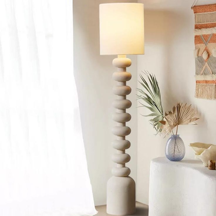 a white table lamp sitting next to a vase with a plant on top of it