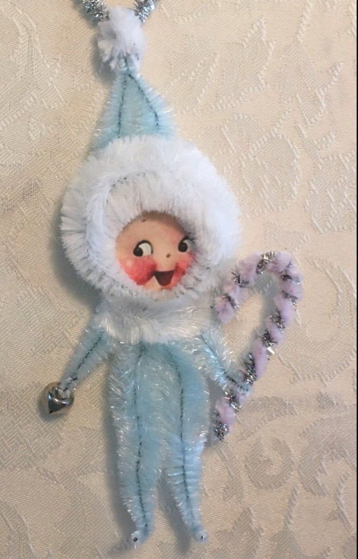 a stuffed doll hanging from a wall on a white fabric covered surface with silver beads