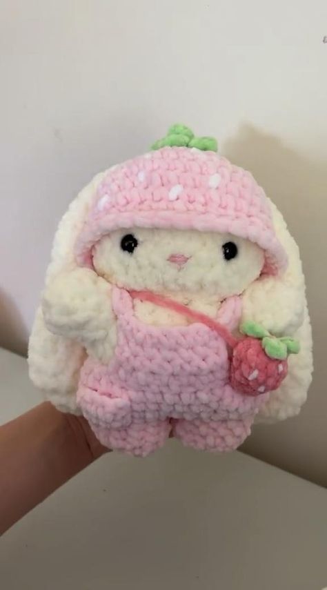 a hand holding a small stuffed animal with a strawberry on it's chest and wearing a pink knitted outfit