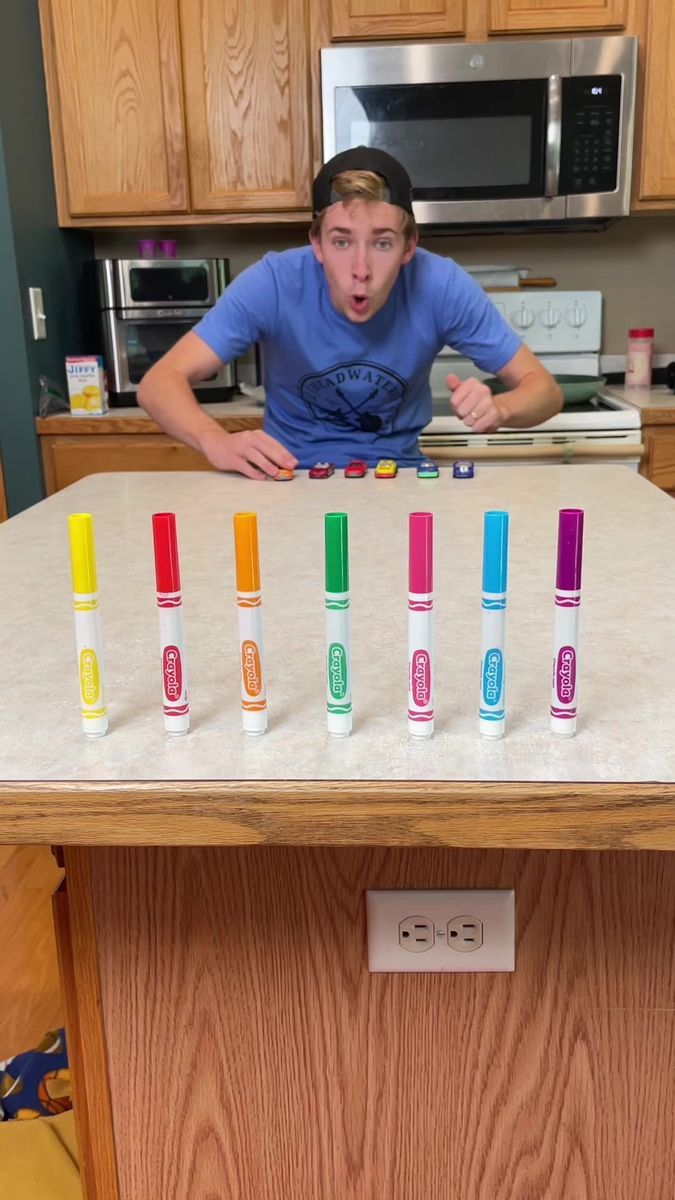 a young man standing in front of a table filled with different colored crayons