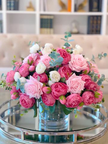 a vase filled with pink and white flowers sitting on top of a glass table next to a couch