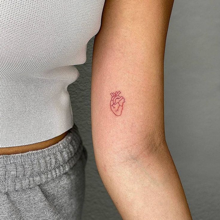 a woman's arm with a small red heart tattoo on the left side of her arm