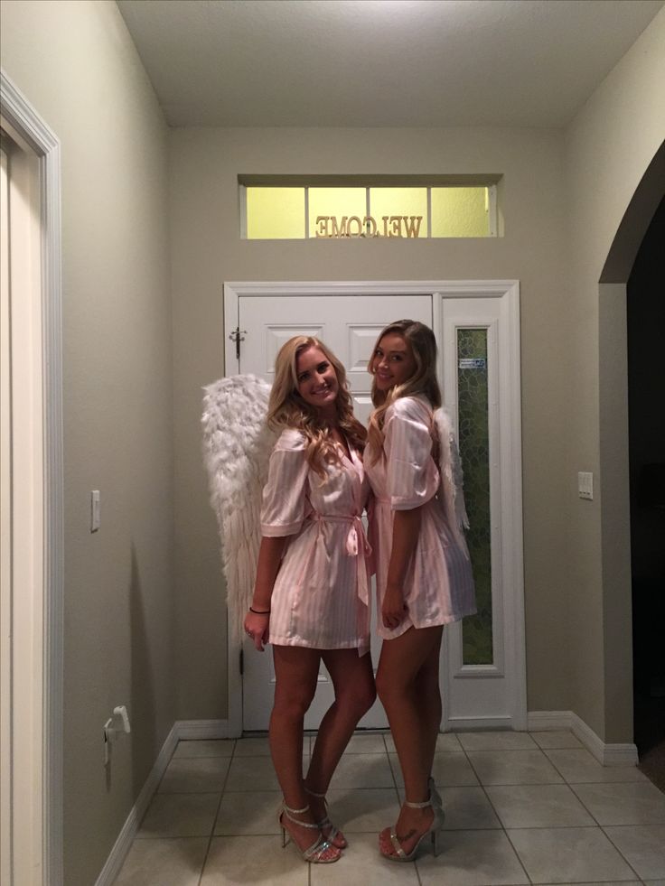 two beautiful young women standing next to each other in front of a door with angel wings