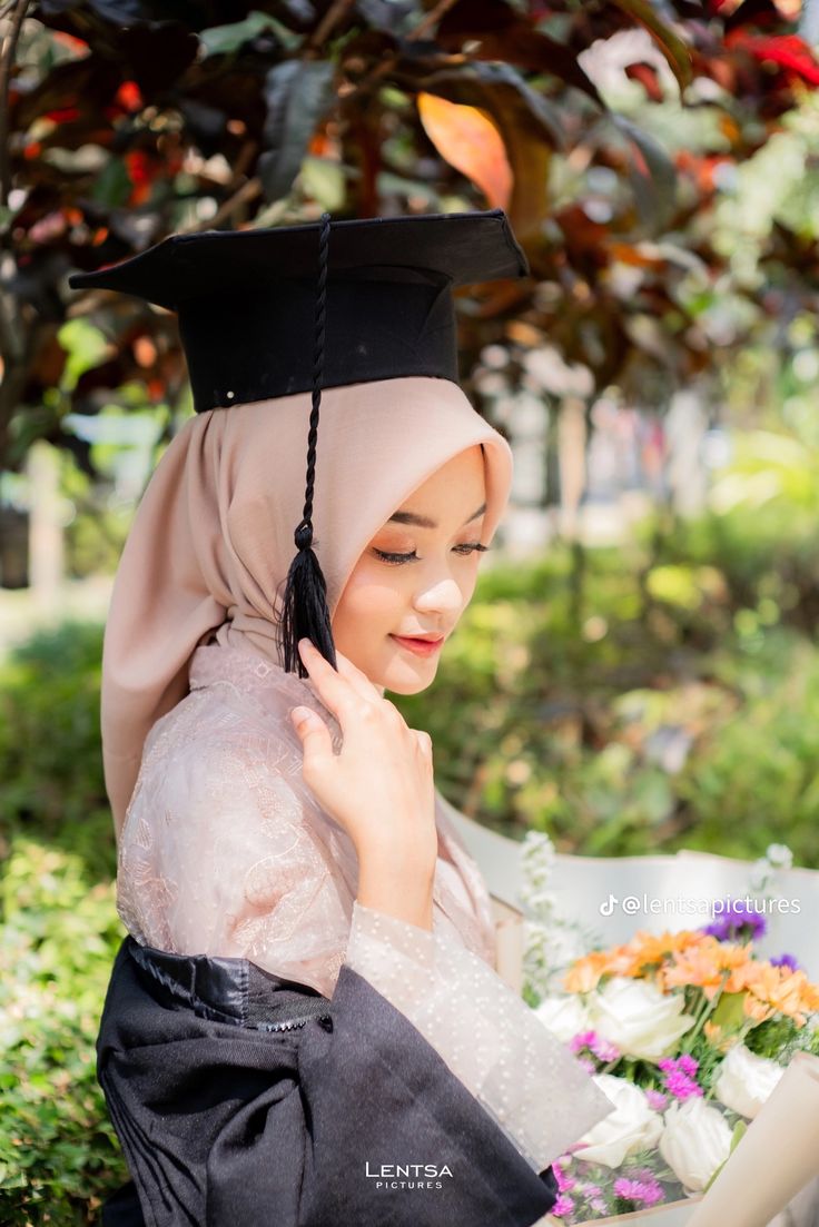 a young woman wearing a graduation cap and gown sitting under a tree with flowers in the foreground