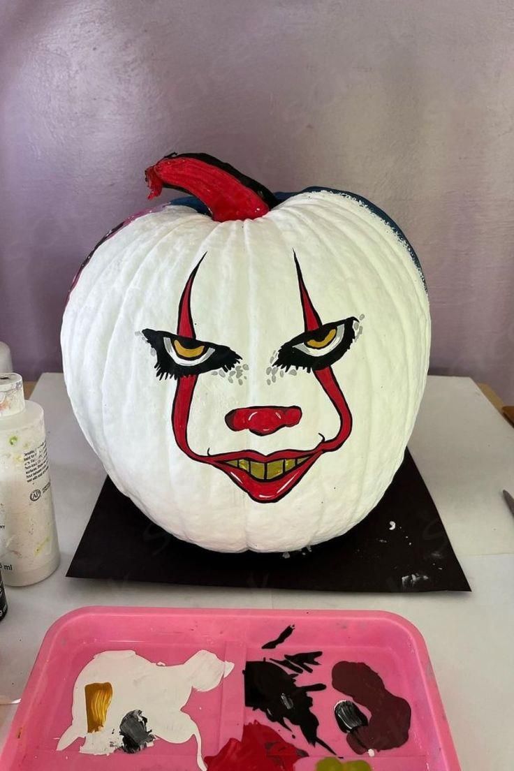 a white pumpkin with red and black face painted on it next to a pink tray