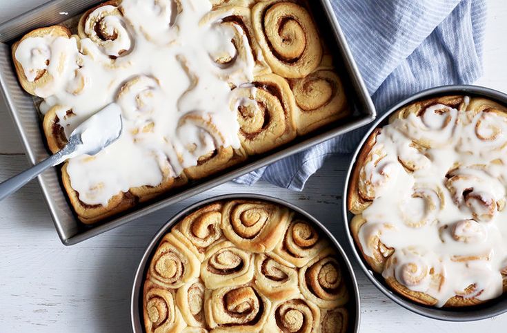 two pans filled with cinnamon rolls covered in icing