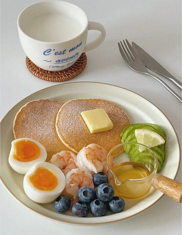 a plate with pancakes, eggs and fruit on it next to a cup of coffee