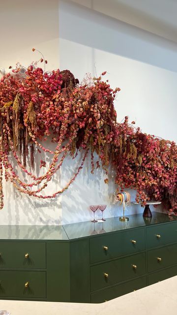 an arrangement of dried flowers on display in a room with green drawers and dressers