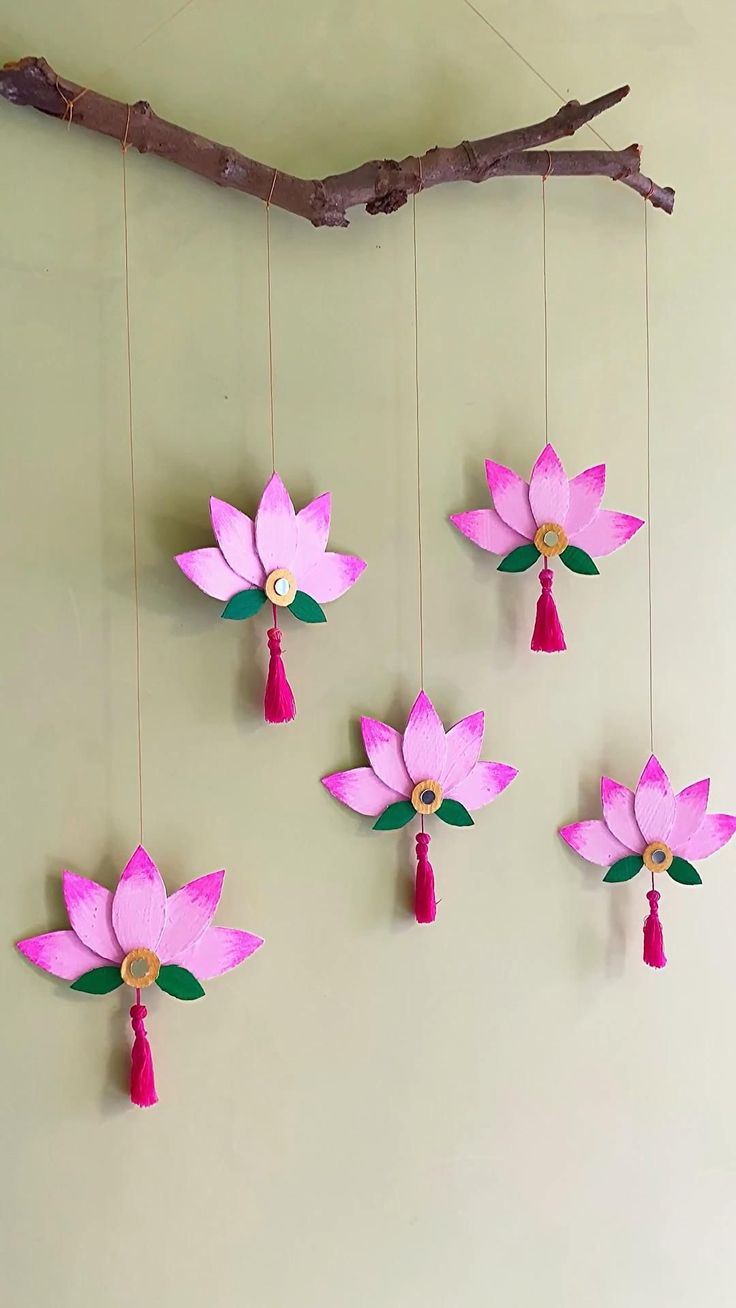 pink paper flowers hanging from a branch with tassels attached to the ends and two red tassels on each end