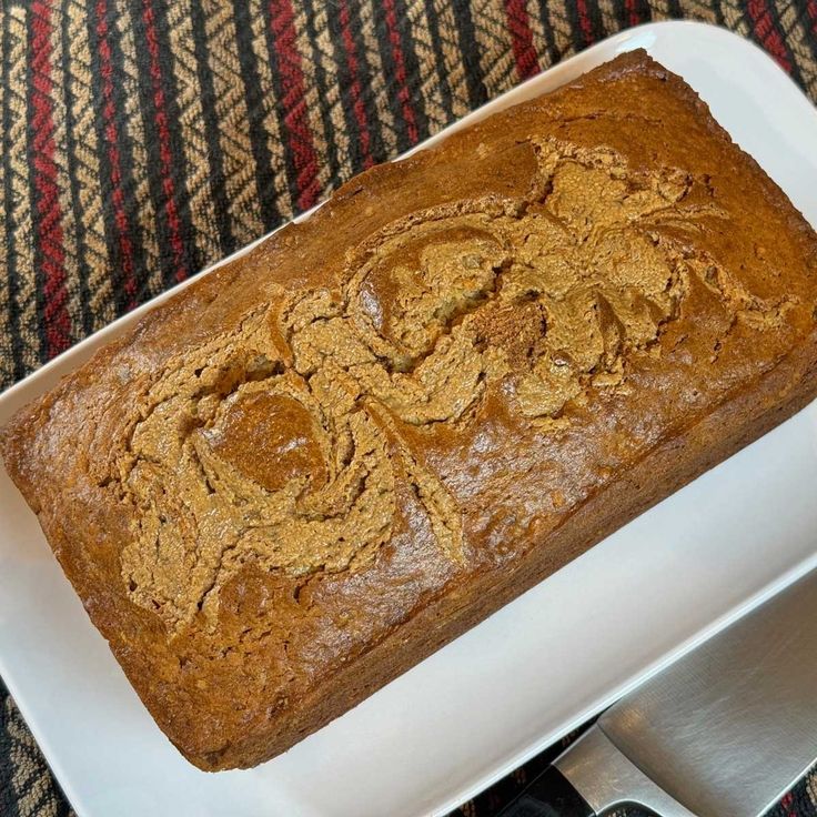 a loaf of bread sitting on top of a white plate next to a knife and fork