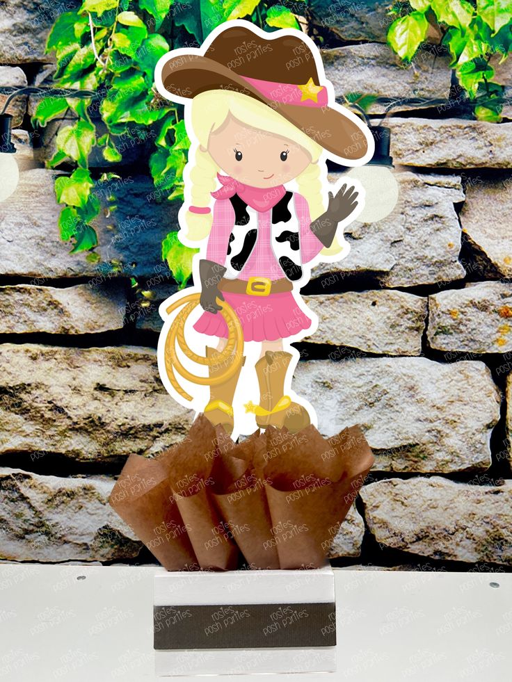 a paper cutout of a girl with a cowboy hat and lasso standing on top of a rock wall