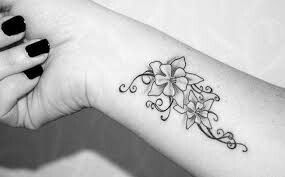 a black and white photo of a flower tattoo on the left arm with swirls around it