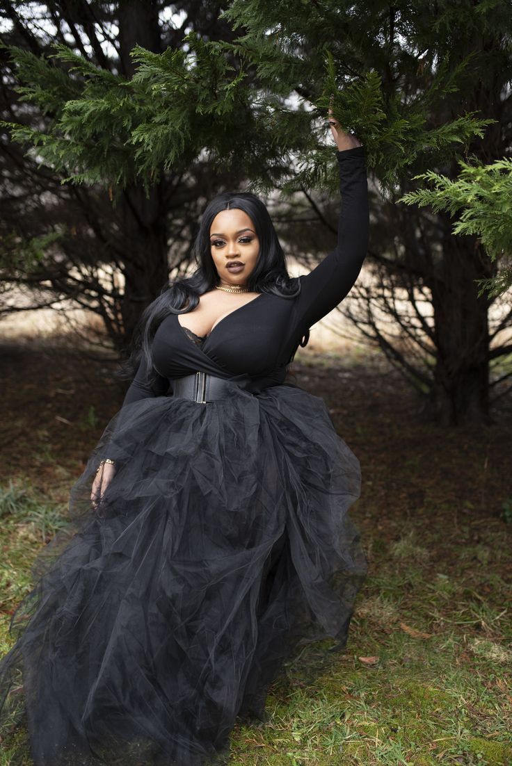 a woman in a black dress is posing for the camera with her arms up and hands behind her head