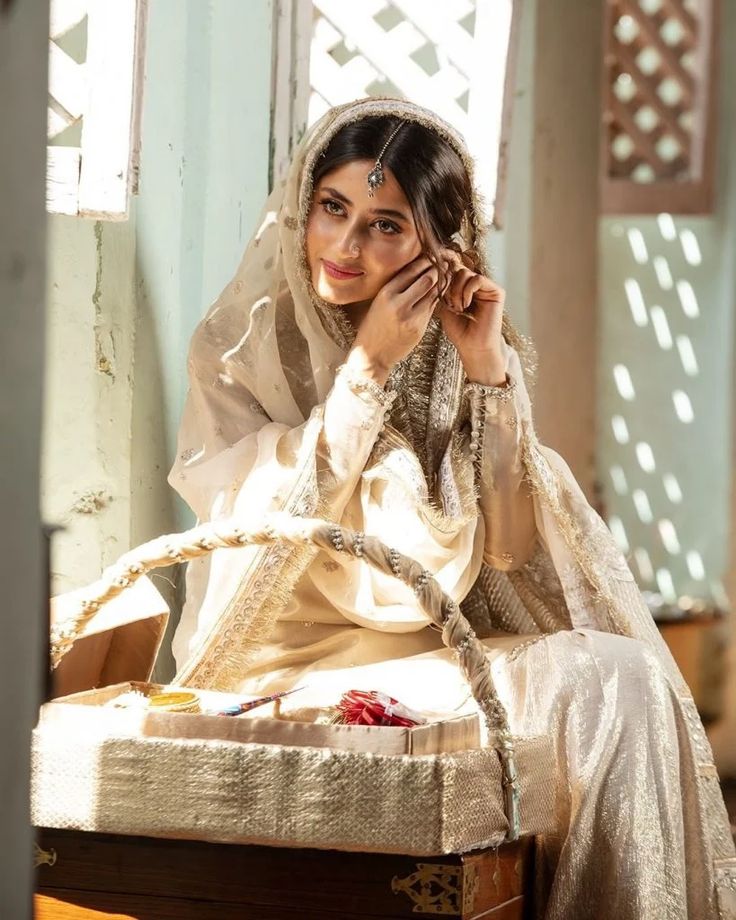 a woman sitting on top of a wooden chair in a white dress and head scarf