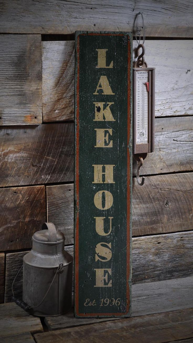 a sign that says lake house hanging on a wall next to a watering can and an old fashioned thermometer