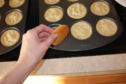 a person holding a cookie in front of some muffins on a baking sheet