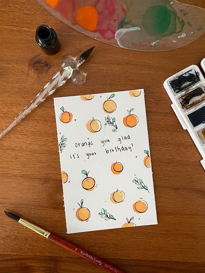 a card with oranges on it next to some watercolor paints