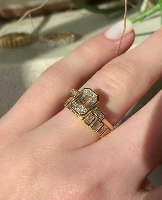 a woman's hand holding a gold ring with two diamonds on the middle and sides