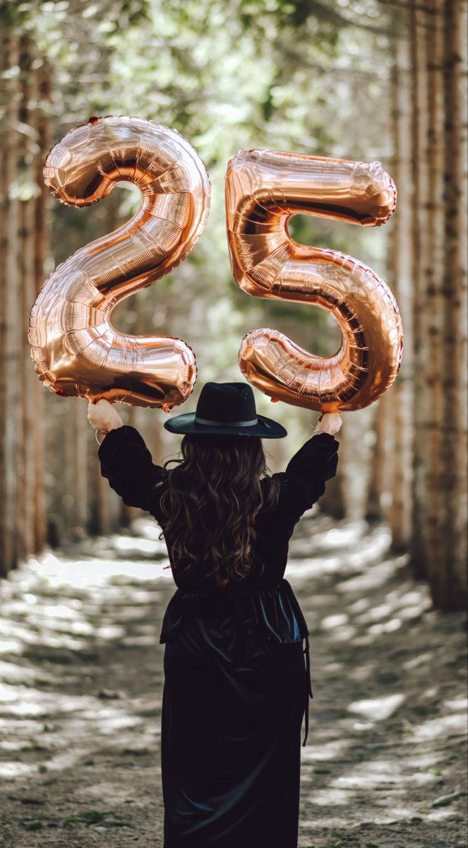 a woman in a hat is holding up the number twenty five balloons that spell out 25