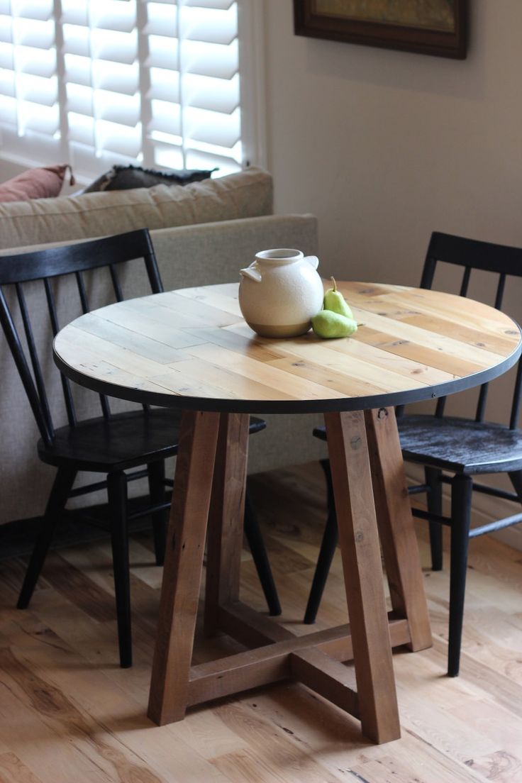 a wooden table with two black chairs and a white vase sitting on top of it