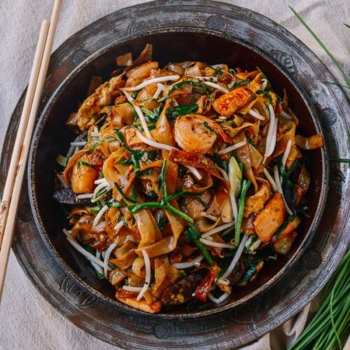 a bowl filled with shrimp and vegetables next to chopsticks on top of a table