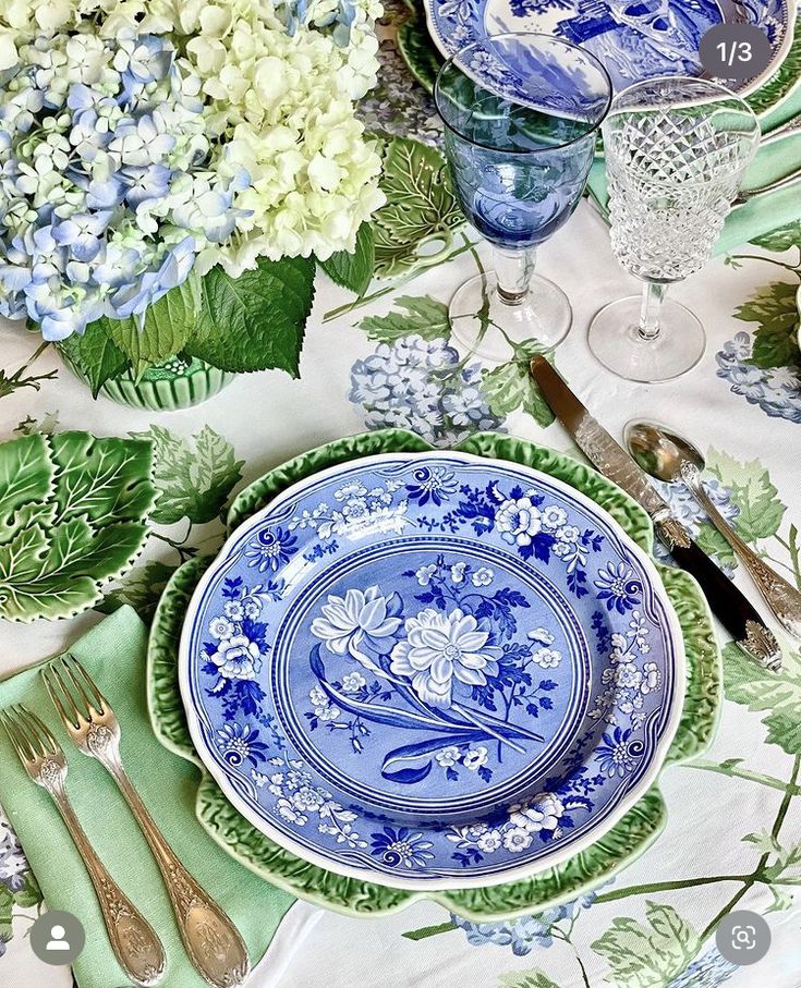 the table is set with blue and white plates, silverware, and flowers on it