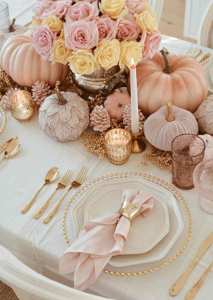 the table is set with pink and yellow flowers, goldware, silverware, and candlesticks