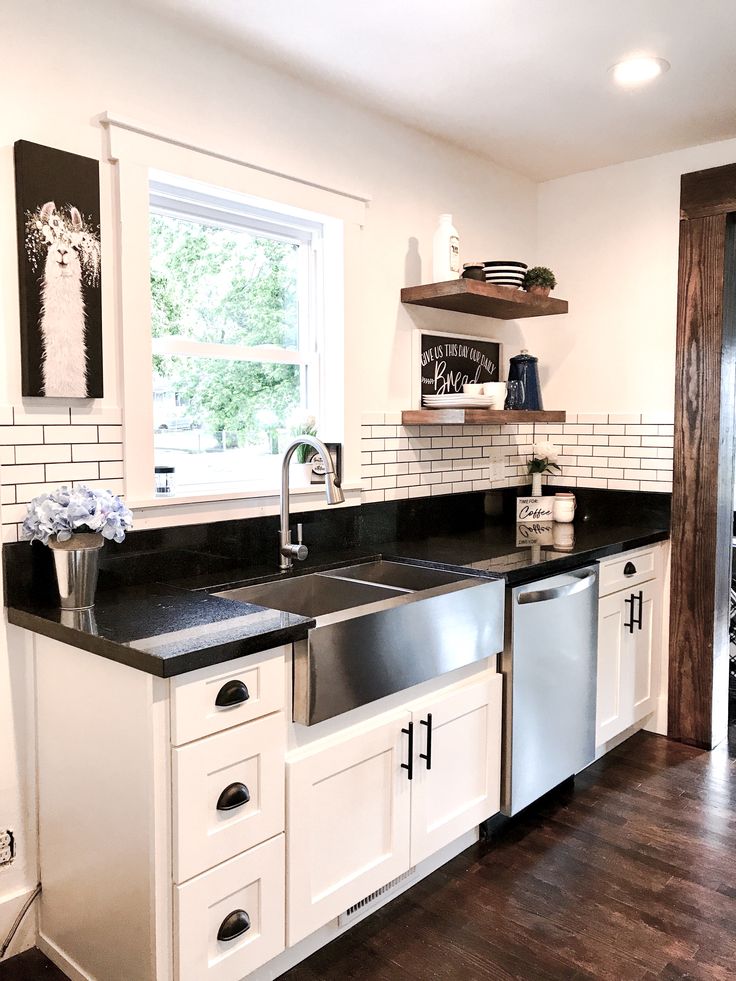 a kitchen with white cabinets and black counter tops, wood flooring and open shelving