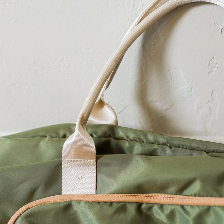 a green duffel bag with a white handle hanging from it's side on a wall