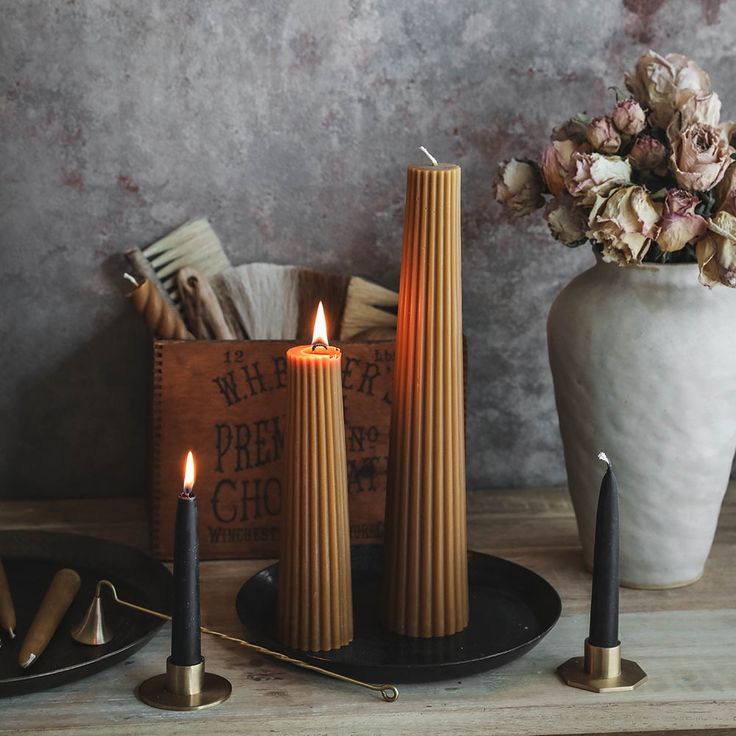 three candles are sitting next to each other on a table with flowers in a vase