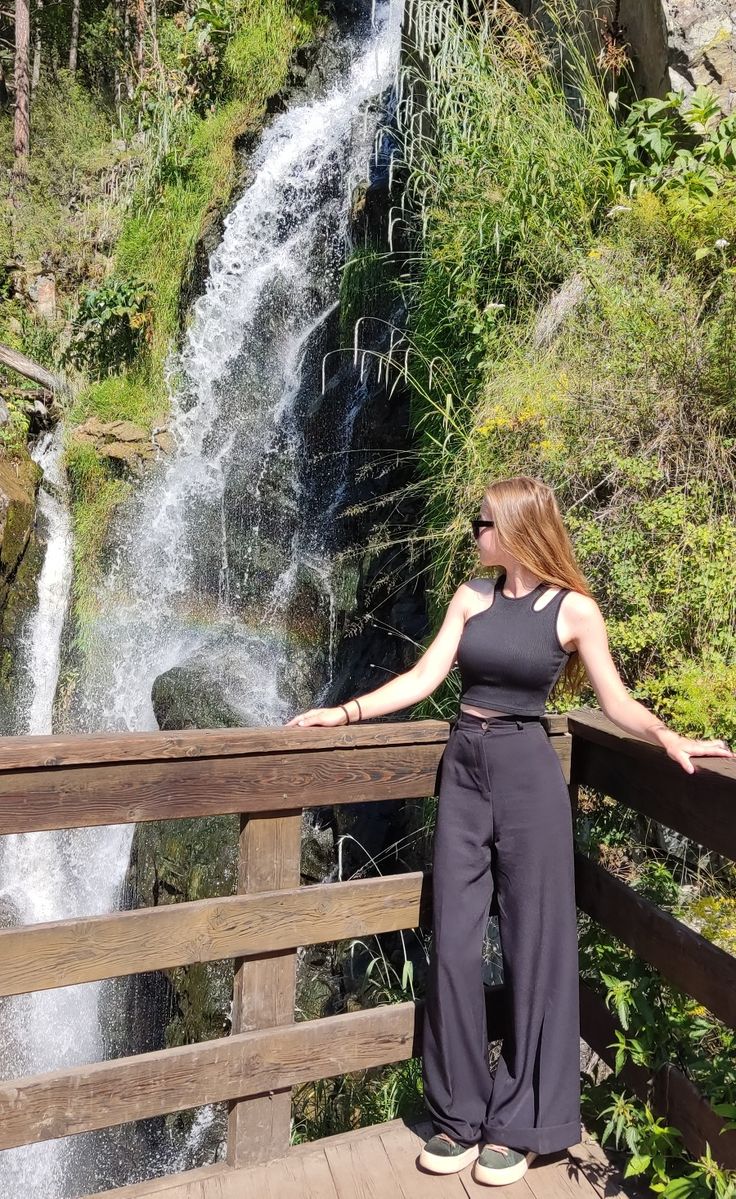 a woman standing on a bridge looking at a waterfall