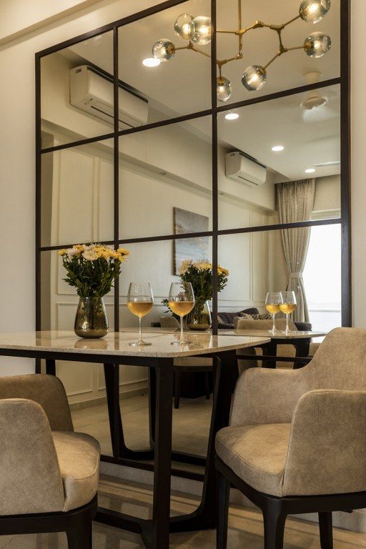 a dining room table with chairs and a large mirror on the wall above it that has flowers in vases