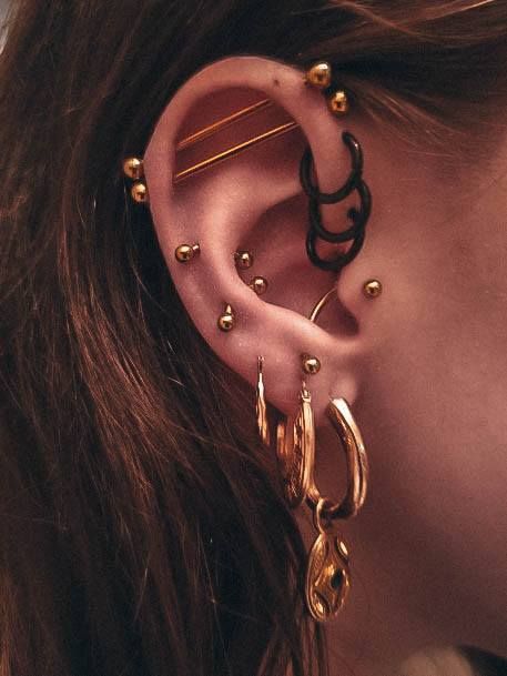 a close up of a person with ear piercings on their ears and wearing gold earrings