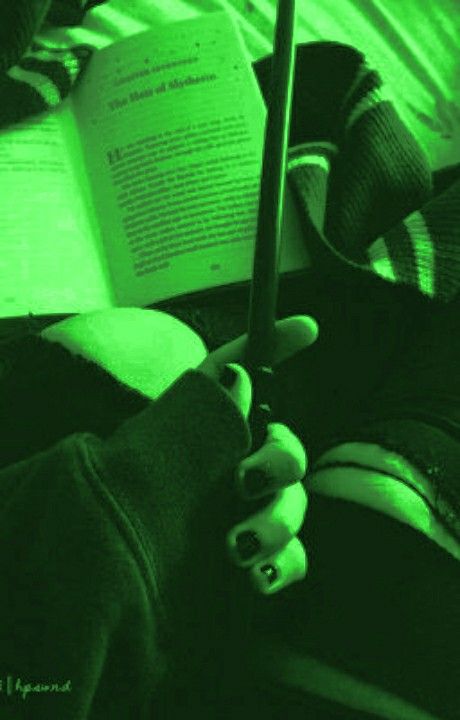 a person is holding an open book in their hand while sitting on a bed with green light