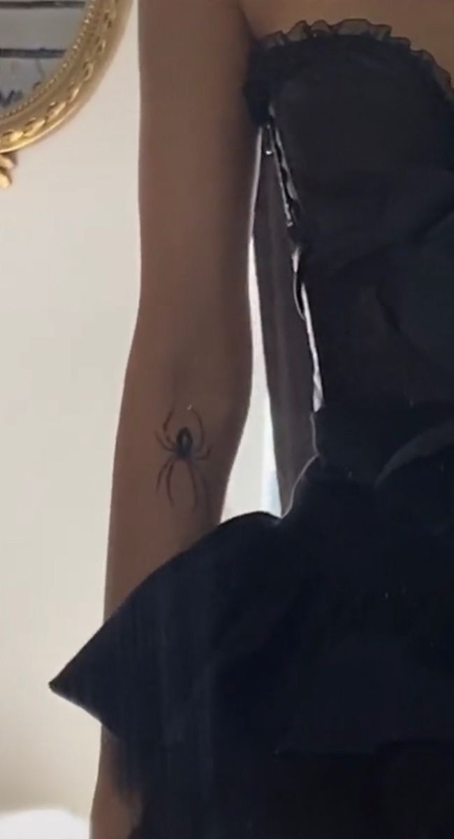 a woman wearing a black dress with a spider tattoo on her left arm and leg