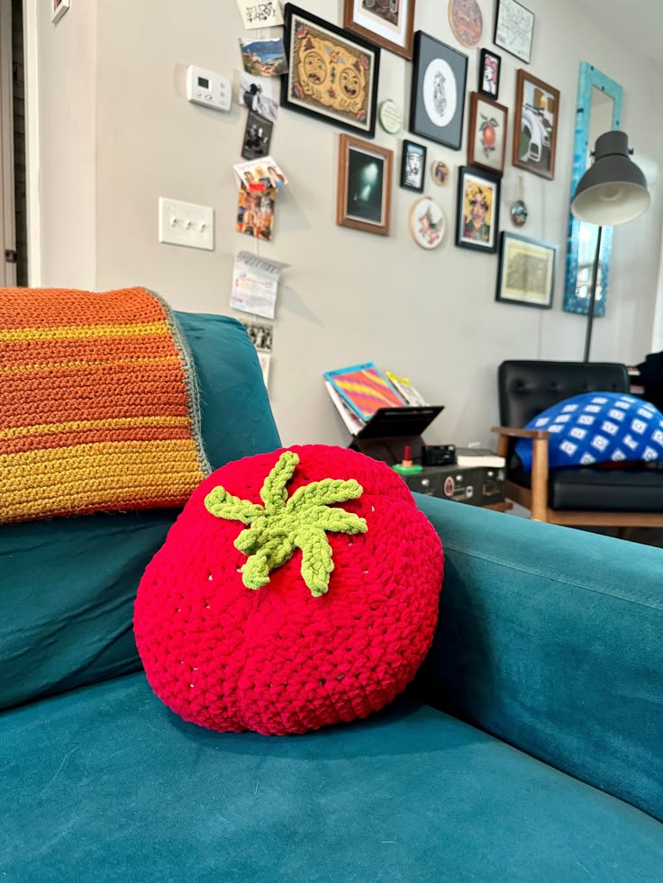 a red knitted strawberry pillow sitting on top of a blue couch in a living room