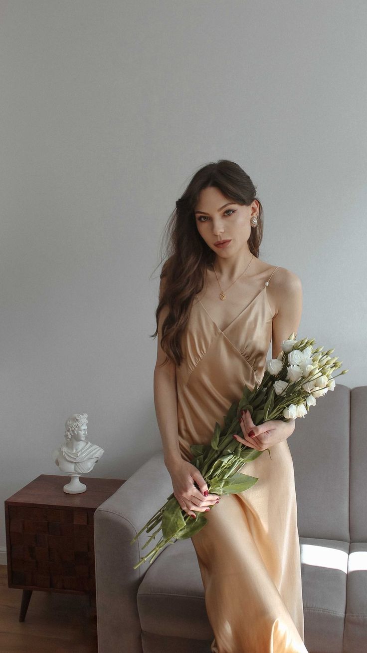 a woman is sitting on a couch with flowers in her hand and wearing a dress