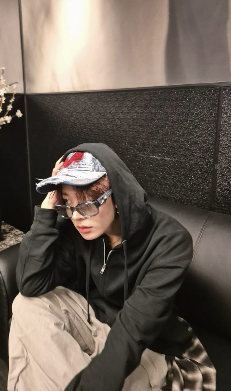 a person sitting on a couch wearing glasses and a hoodie over their head,