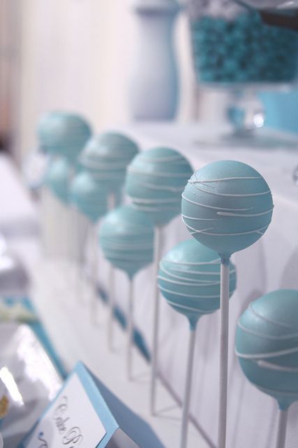 blue cake pops are lined up on a table with white plates and silverware in the background