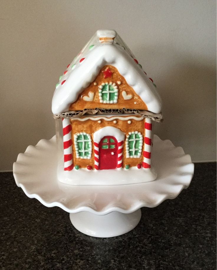 a white plate topped with a small gingerbread house on top of a cake stand