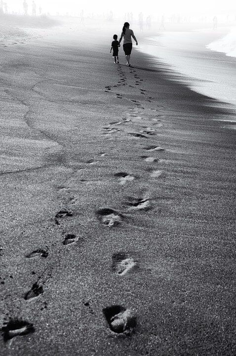 two people are walking on the beach with footprints in the sand and one is carrying a child's hand