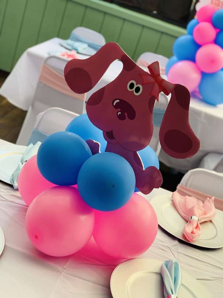 there is a dog balloon on top of the table at this birthday party with blue, pink and white balloons