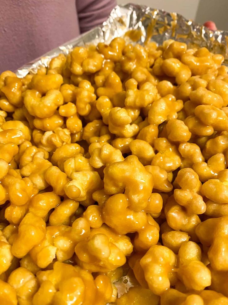 a person holding a tray full of caramel coated popcorn kernels in their hands