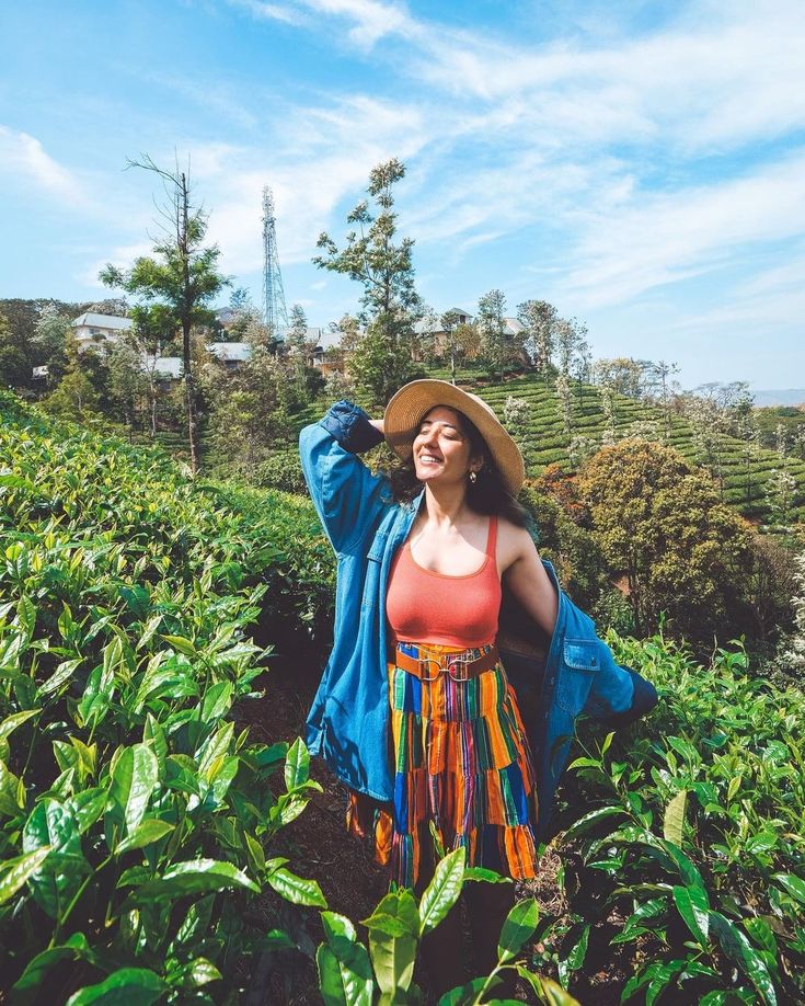 a woman standing in a field with her arms behind her head and wearing a hat