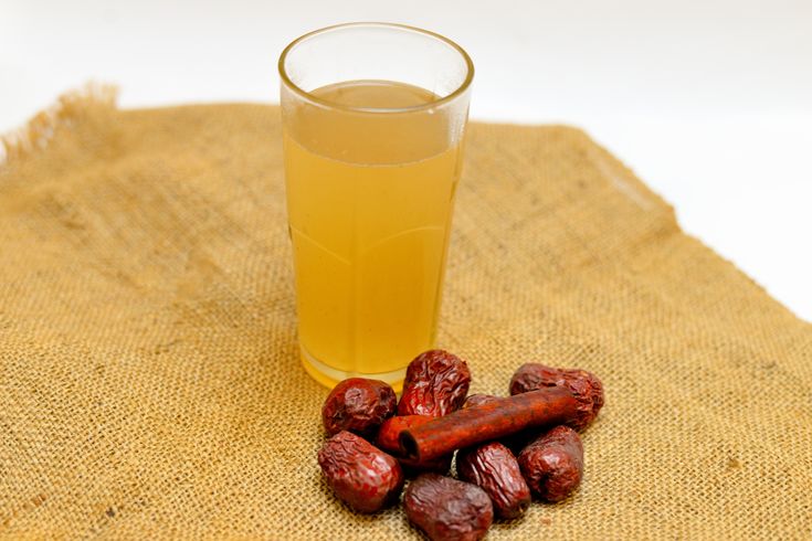 a glass filled with liquid next to some peanuts on a burlap table cloth