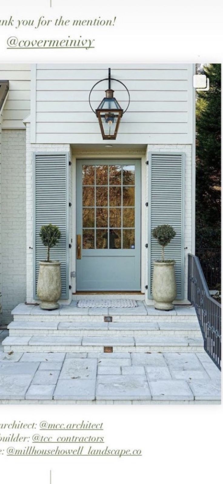 the front door of a white house with two planters and a light fixture above it